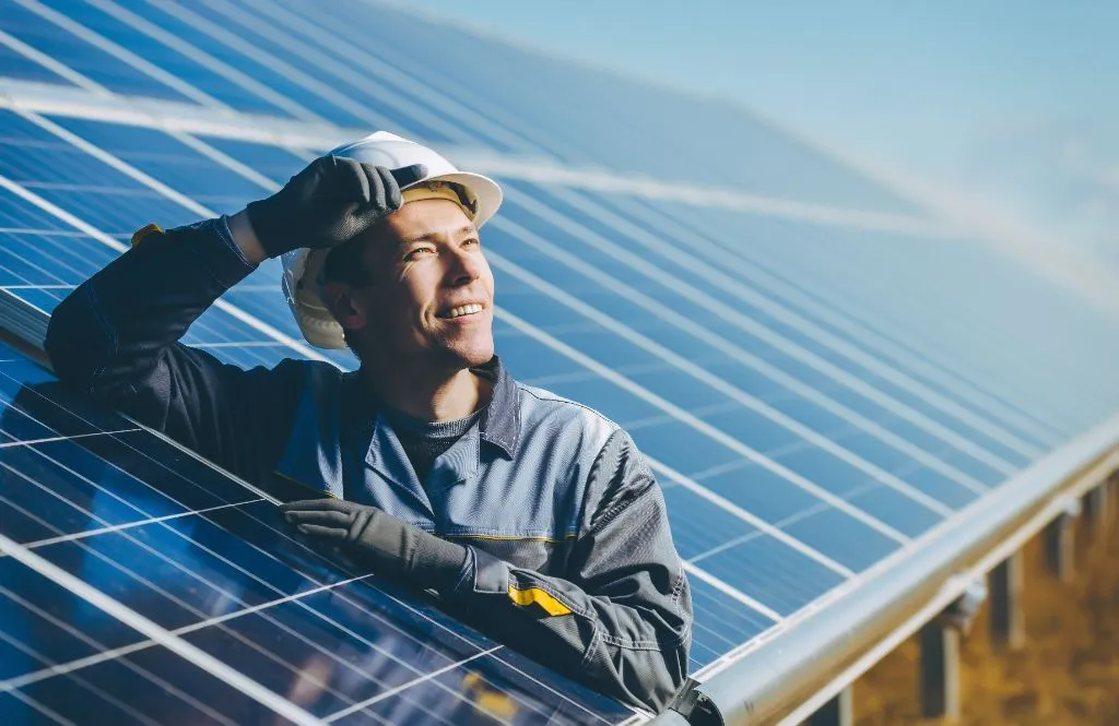 Portrait of a happy solar technician near rows of solar panels.