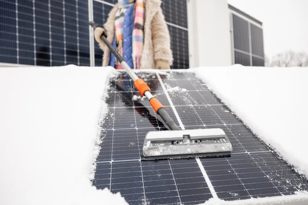 How Does Snow On Solar Panels Affect Systems’ Productivity? 3 Woman cleans solar panels from snow on the roof of her house.